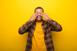 Young african american man on vibrant yellow background covering eyes by hands. Surprised to see what is ahead