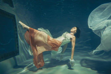 Wall Mural - elegant slender girl swims underwater like a free diver in a white evening dress with beautiful fabric