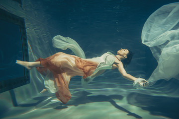 Wall Mural - elegant slender girl swims underwater like a free diver in a white evening dress with beautiful fabric