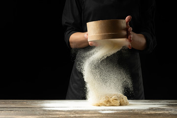 A professional chef in a professional kitchen prepares dough from flour to cook Italian pasta, pizza, the concept of nature, Italy, diet and biology. On a dark background. Design text placement