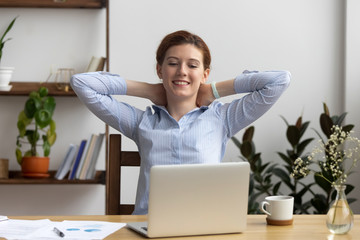 Businesswoman sitting at office desk hold hands behind head relaxing feels good. Positive company member resting accomplished work has a good result looking at computer screen reading pleasant email