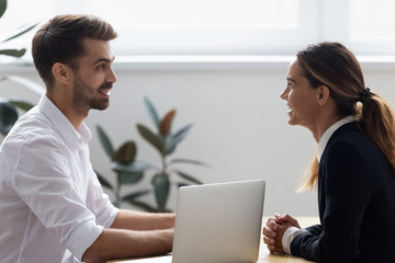 Side view mixed race attractive female in formal suit sitting at desk looking at business partner investor talking in meeting discussing working moments or diverse businesspeople during job interview.