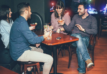 Happy friends drinking cocktails inside jazz cocktail bar - Millennial young people having fun and laughing together in british pub - Friendship, nightlife and youth lifestyle holidays