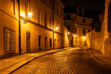 Narrow Cobbled Street In Old Medieval Town With Illuminated Houses By Vintage Street Lamps, Novy Svet, Prague, Czech Republic. Night Shot.
