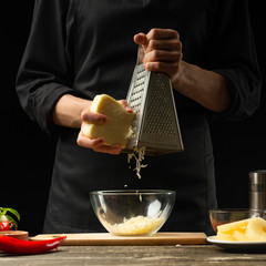 The chef prepares mozzarella cheese, cheddar for Italian pizza, pasta. On a black background, freezing in motion. A concept of tasty and healthy food. Design text, recipe book