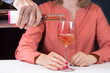 Kobieta siedzi przy stole i trzyma w dłoni kieliszek do wina. Męska dłoń nalewa wina z butelki do kieliszka.
