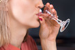 Biała młoda kobieta trzyma kieliszek do wódki przystawiony do ust i pije wódkę.