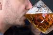 Twarz białego mężczyzny z lekkim zarostem pijącego jasne piwo z kufla.