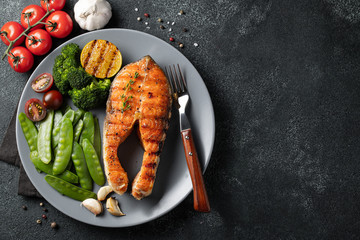 Wall Mural - Tasty and healthy salmon steak with green peas, broccoli and tomatoes on a gray plate. Diet food on a dark background with copy space. Top view. Flat lay