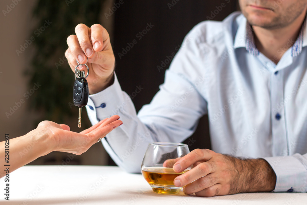 Piłeś nie jedź. Mężczyzna w jasnej koszuli siedzi przy stole ze szklanką whisky. Oddaje kobiecie kluczyki do auta. - obrazy, fototapety, plakaty 