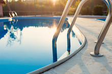 Close-up Of A Part Of Swimming Pool With A Stainless Steel Ladder And Blue Water On Sunset. Summer Vacation, Holidays, Relax, Summer Activities Concept