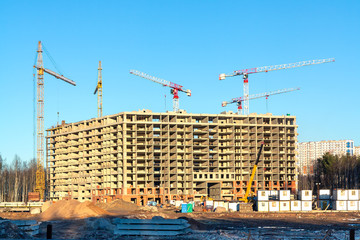 Construction of a new multi-storey building surrounded by forests. Construction cranes against the blue sky.