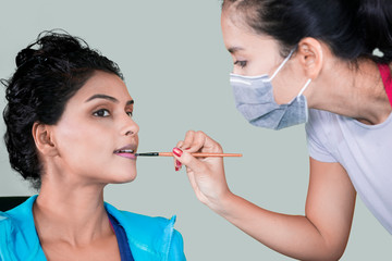 Wall Mural - Female makeup artist using a brush to apply lipstick