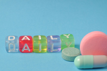 Word DAILY  from the letters of cubes and medical pills. Colored pills and capsule on blue background. Pharmacy Theme,