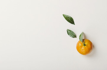 One orange sweet tangerine with green leaves on white background. Copy space, top view, flat lay