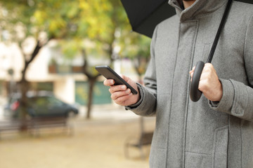 man hand holding phone and umbrella in the street