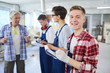 © pressmaster - Content excited handsome young carpentry worker in gloves standing in row of interns at construction site and making notes in clipboard while smiling at camera