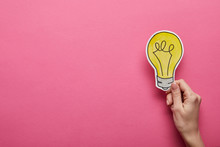 Top View Of Hand Holding Yellow Light Bulb On Pink Background