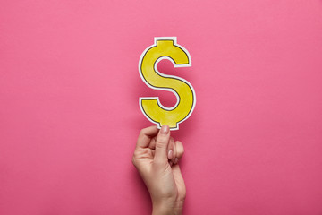 top view of hand holding yellow dollar sign on pink background