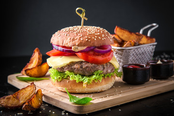 Fresh tasty burger with beef cutlet and fried potatoes on black background