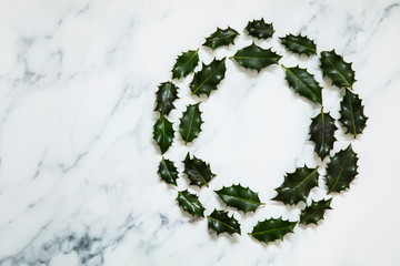 Wall Mural - Christmas layout made from festive holly leaves on a white marble background