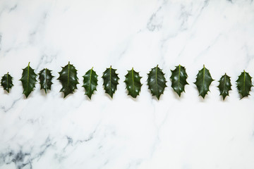 Wall Mural - Christmas layout made from festive holly leaves on a white marble background