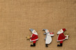 2 Weihnachtsmänner und Schneemann mit Stern und Geschenken Ornamente aus bemaltem Holz auf Hintergrund aus Jute grosses Textfeld