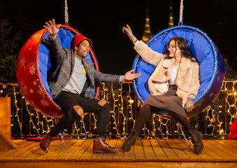 Wall Mural - Couple posing for funny photo on swing chair at Christmas market.