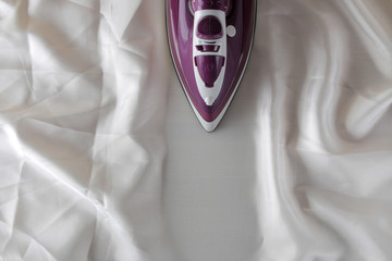 Lilac iron on a piece of white crumpled fabric. ironing clothes. household electrical appliances. view from above.