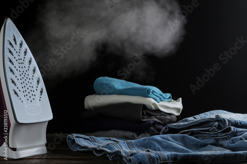 Fotografía lilac iron releases steam and a stack of clothes on a black background