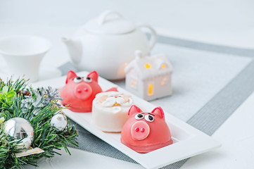 Marzipan in the shape of the symbol of the new year pink - a pig, sweet delicate macaroons, marshmallows, peanuts in sugar pastel colors on a light background.