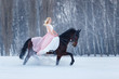 Young woman in dress riding horse on winter field
