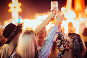 Female friends cheering with beer at music festival