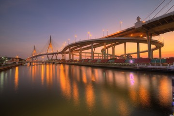 Wall Mural - Low angle view of Bhumibol Suspension Bridge (or Industrial Ring Road ) over Chao Phraya River under evening twilight in Bangkok Thailand, with beautiful reflections on smooth water at red rosy dusk