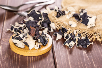 Lot of slices of dry black mushroom jew ear variety on round bamboo plate on brown wood