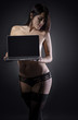 © Vitte Yevhen - Sexy young brunette woman in black sensual lingerie using laptop and posing on black background wall in studio.