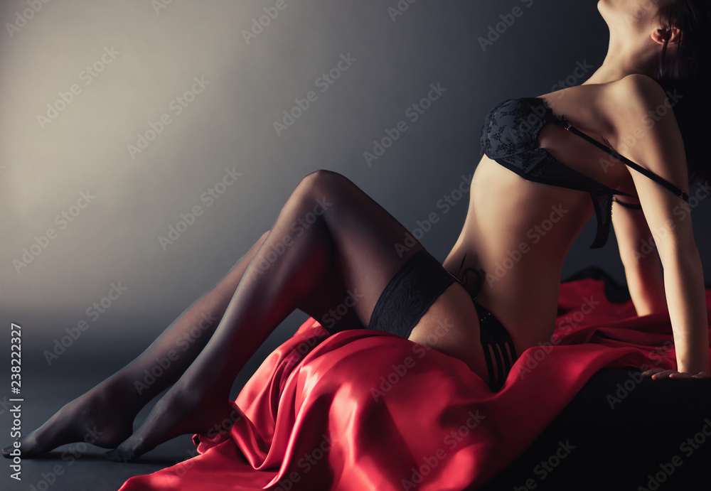 Sexy young brunette woman in black sensual lingerie and in stockings posing on bed in studio. - obrazy, fototapety, plakaty 