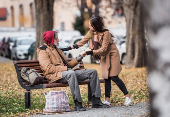 Wall Mural - Young woman giving food to homeless beggar man sitting on a bench in city.