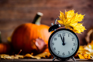 Vintage alarm clock and maple tree leaves with pumpkins on yellow wooden background with bokeh. Autumn season image style for Thaksgiving holiday