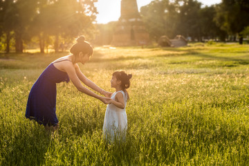 young asia mother having fun with daughter in field with sunlight on grass