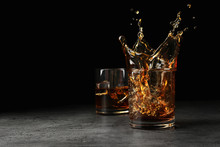 Splashing Golden Whiskey In Glass With Ice Cubes On Table. Space For Text