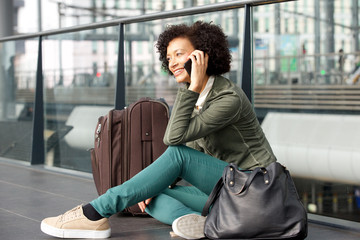 Wall Mural -  african american woman sitting on floor at station with luggage and talking on cellphone