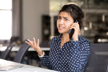 Outraged attractive Indian female employee talking by phone, arguing with client or customer, actively gesticulating, businesswoman having serious conversation on smartphone, solve business problem