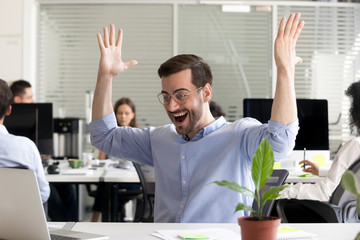 Wall Mural - Excited happy satisfied businessman with raised hands celebrating business achievement at workplace, looking at laptop screen, receive good news, results, corporate success, motivated by victory