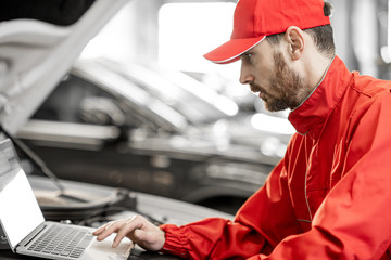 Wall Mural - Handsome auto mechanic in red uniform doing engine diagnostics with computer in the car service