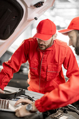 Wall Mural - Two auto mechanics in red uniform doing engine diagnostics with computer in the car service