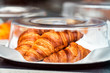 © Kristina Blokhin - Closeup of golden orange baked pastry croissant large fresh in bakery cafe on tray covered with glass plastic cover on rertail window display, catering breakfast