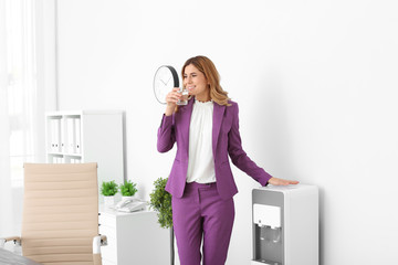 Woman having break near water cooler at workplace. Space for text