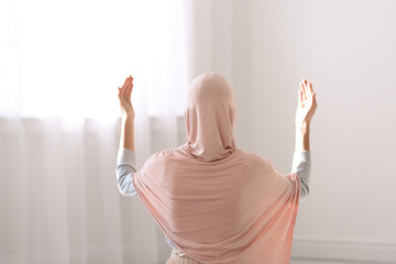 Young Muslim woman in hijab praying indoors