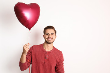 Portrait of young man with heart shaped balloon on white background. Space for text